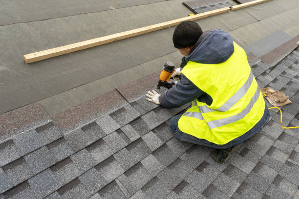 v5 Qualified workman in uniform work wear using air or pneumatic nail gun and installing asphalt or bitumen shingle on top of the new roof under construction residential building
